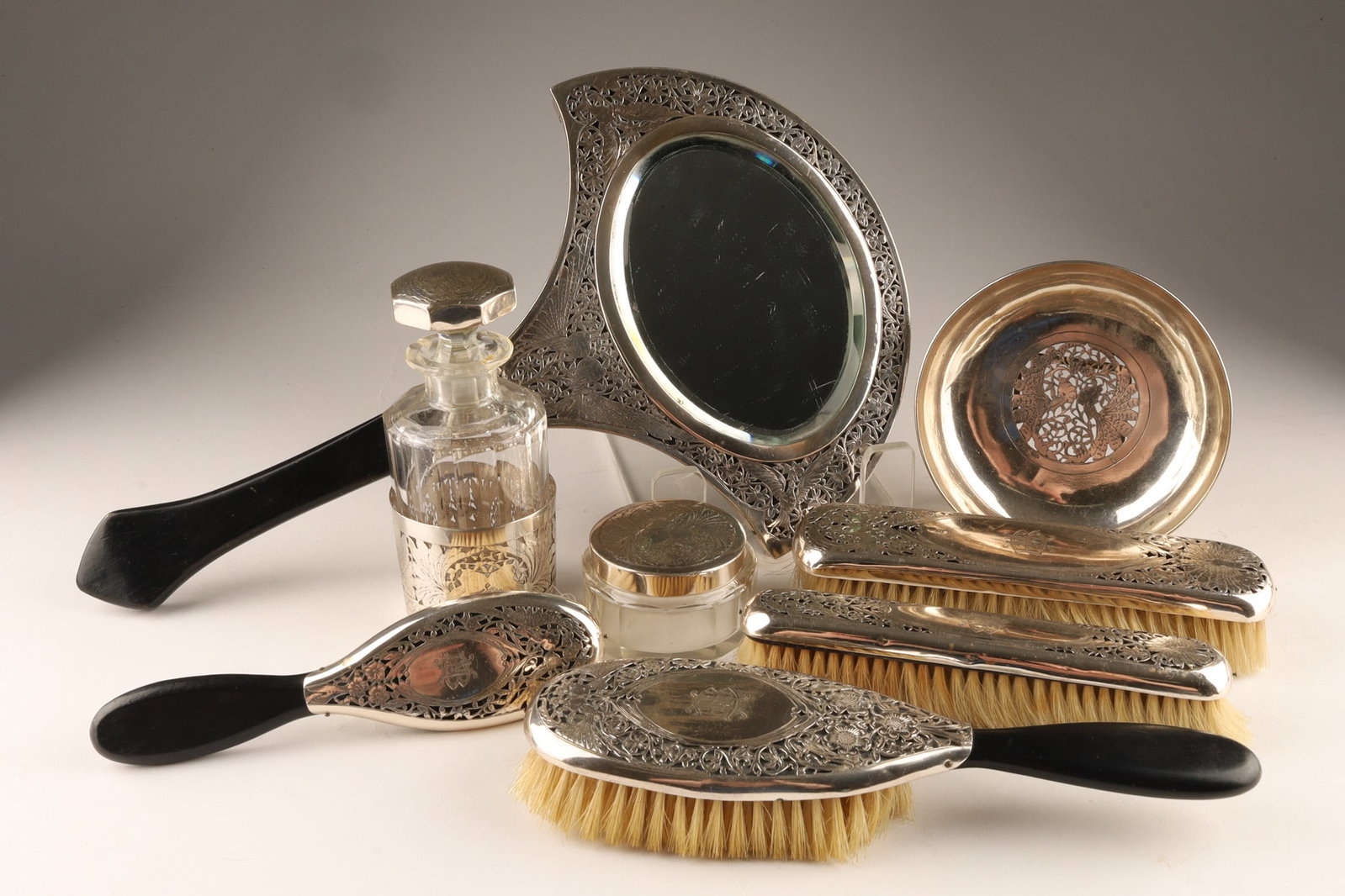 Dutch Art Deco Silver and Crystal Vanity Set with Reticulated Bird Motifs: An elegant antique Dutch Art Deco sterling silver and cut-crystal vanity dressing table set, featuring intricate repousse filigree ornamentation throughout. The comprehensive lot includes a striking c