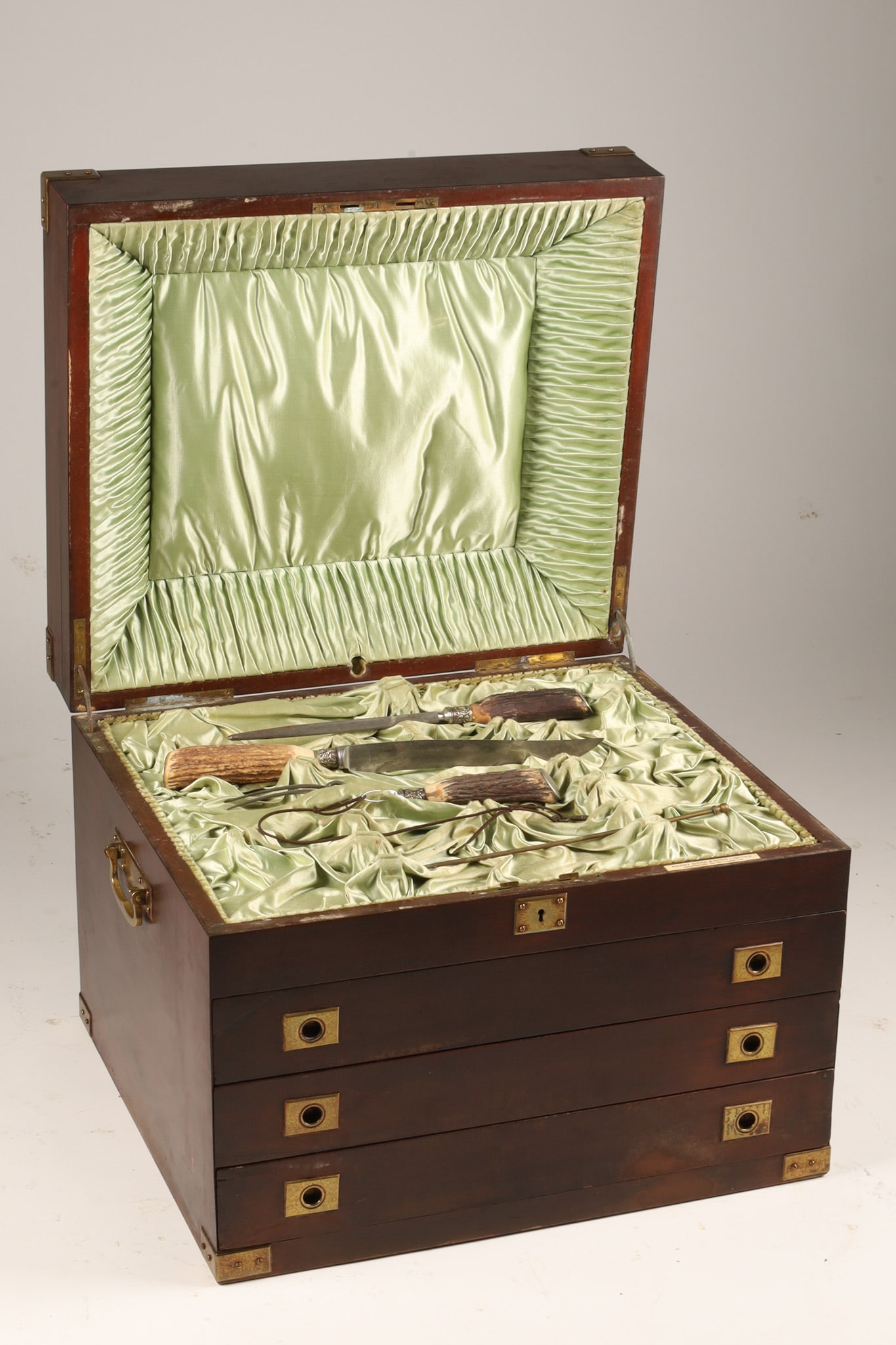 Henry Birks and Sons Mahogany Campaign Style Silverware Chest: Henry Birks and Sons mahogany campaign style cutlery chest, featuring a hinged top lid opening to a ruched green satin-lined interior compartment above three graduated drawers. Styled with brass flush