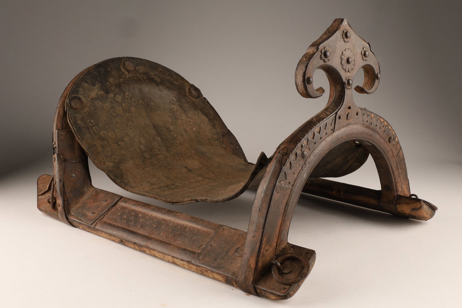 Antique Middle Eastern Wooden and Metal Camel Saddle Frame: An antique Middle Eastern camel saddle frame, crafted from seasoned hardwood and reinforced with forged iron plates. The piece features a carved rear pommel accented by decorative geometric incised pa
