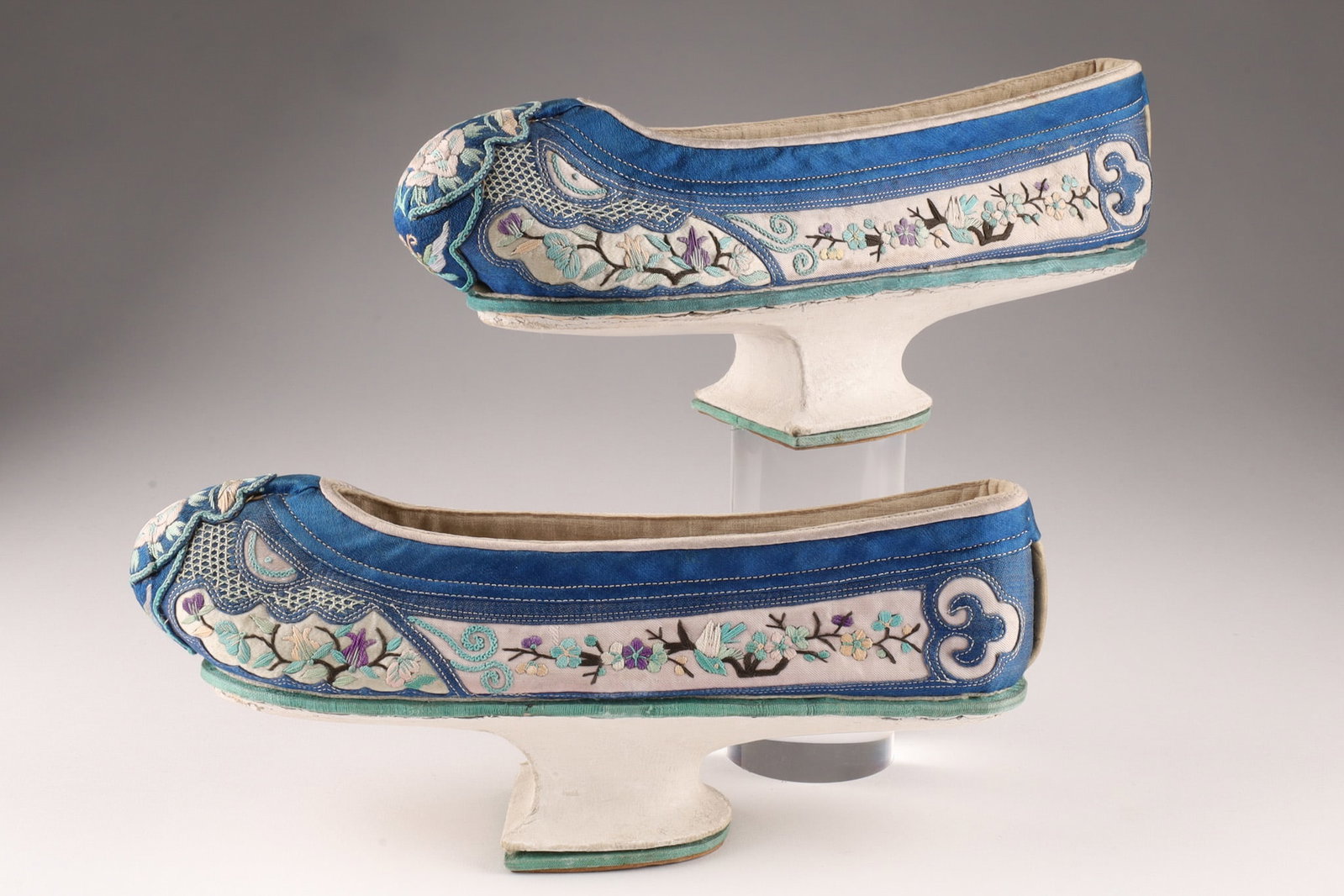 Pair Manchurian Antique Silk Embroidered Woman's Shoes: THE SIMON CHANG COLLECTION - Pair of Manchu woman's shoes, the base with a raised wood sole covered in cotton and then painted, the upper part of blue and grey satin with silk hand embroidered cherry 