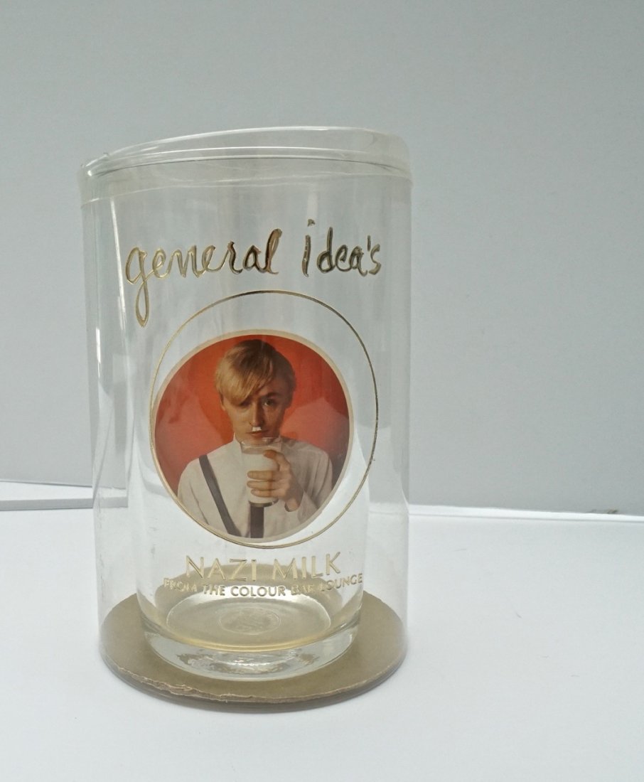 GENERAL IDEA: Nazi Milk, Colour Bar Lounge. 1980. Drinking glass with offset label in plastic container with gold hot-stamping. Signed on bottom in marker. 6" x 4"