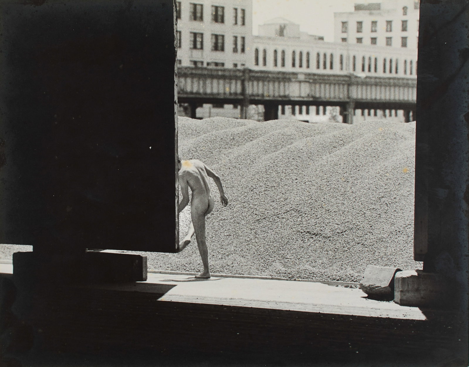 Jack Dowling (American, 1931-2021): Piers, 1974. Gelatin silver print, backed by illustration board. A compositionally breathtaking photo of a nude male model standing at the West Side Piers in New York City. This photograph was