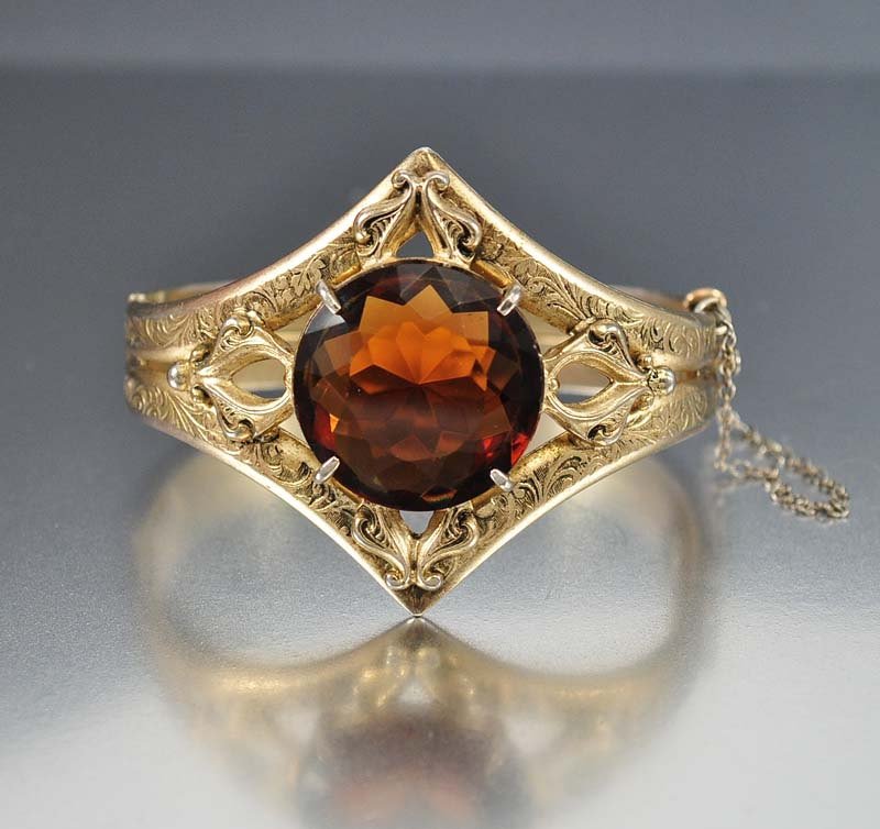 Bold and impressive late Art Deco bangle bracelet with : bold and impressive late art deco bangle bracelet with a large topaz glass stone set in a diamond shape frame. the gold washed band has an elaborate embossed design with the open back topaz stone flan