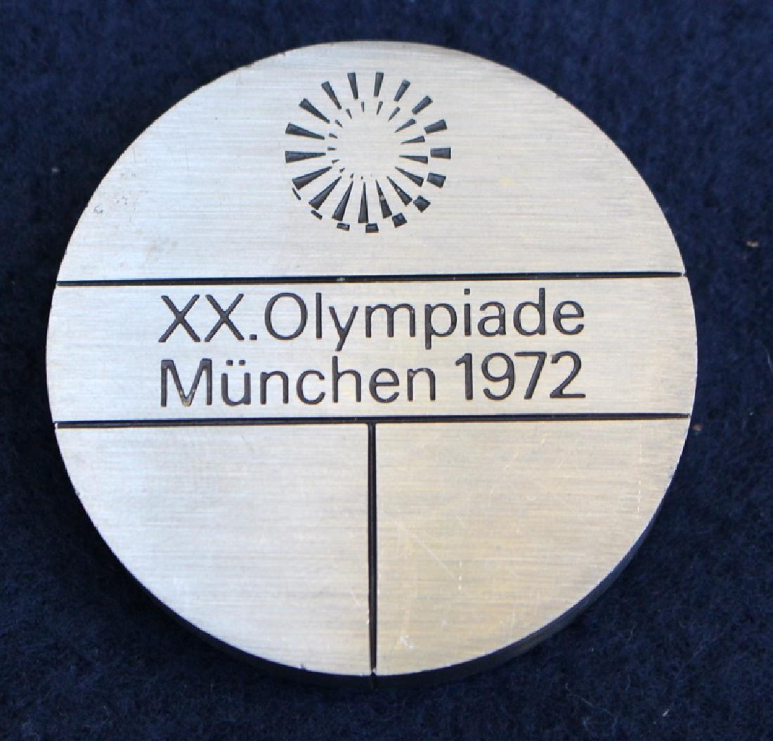 1972 Munich Summer Olympics Partication Medal.: Made from stainless steel, the 1972 participation medal was a very simple design from Fritz Koenig. The obverse shows the Munich Olympic emblem over 2 lines of text. The reverse shows the Olympic ring