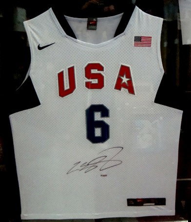 Lebron James Autographed USA Jersey, UDA: Lebron James Autographed USA Basketball Jersey; signed on the front of the jersey in black sharpie marker; beautiful white USA jersey with red and blue lettering; Size XL; framed in a jersey frame; he