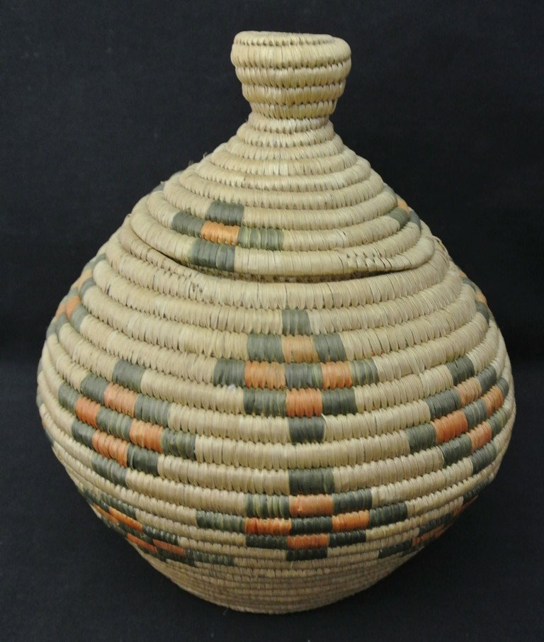 Eskimo Coiled Basket with Lid by Anna Riley of Ste: Eskimo Coiled Basket with Lid by Anna Riley of Stebbins, Alaska. Very good condition with blue and red cross designs. Original tag is included. Measures 8” high x 7.5” in diameter. Circa 1960’s 