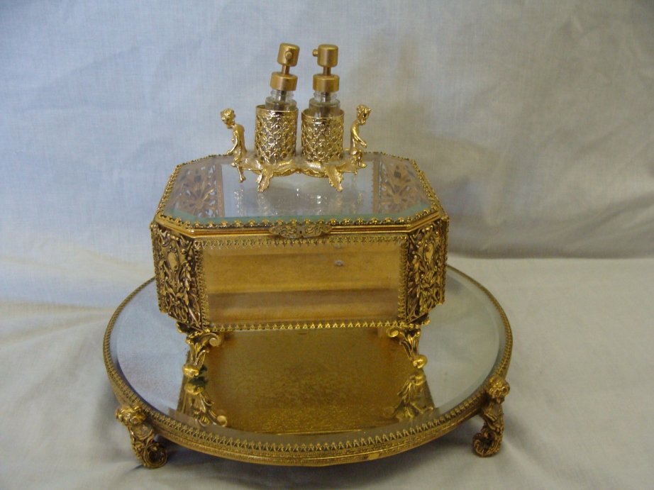 3 PC STYLEBUILT VANITY SET: 10" FOOTED MIRRORED TRAY WITH STYLEBUILT PAPER LABEL ON BOTTOM, 6" X 5" X 3 3/4" TALL DRESSER BOX WITH EMBOSSED STYLEBUILT IN BOTTOM EDGE, CHERUB SMALL TWO BOTTLE PERFUME HOLDER, MIRROR DOES HAVE CLOU