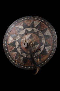 Ornament - Indonesia - Borneo, Dayak: wood, black paint, red and white pigment, of round form, slightly vaulted, carved in bas-relief with radial arranged jagged pattern, animal tail in the centre, two coins attached ("Nederlandsch Indie