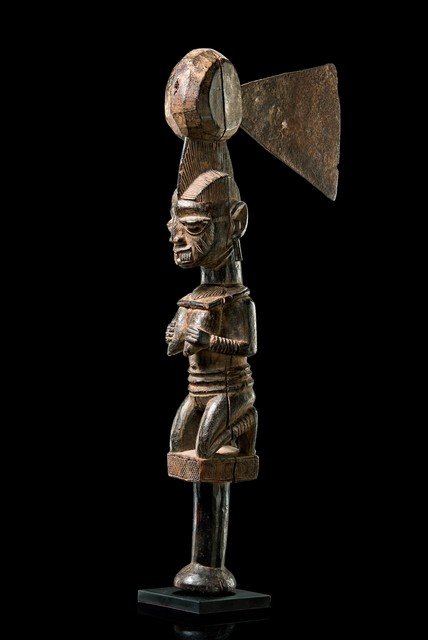 Ceremonial axe "aringo jagun" - Nigeria, Yoruba: wood, partly encrusted, brown patina, kaolin, iron blade, round handle, carved with a kneeling female figure with both hands up to the breasts, head with projection and inserted blade, dam., cracks, t