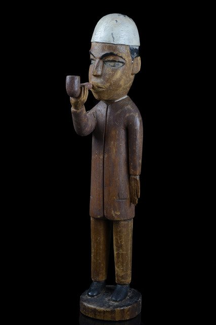 Colon figure: Man with pipe - D. R. Congo, Bakongo: light-weighted wood, matt reddish brown patina, black paint, kaolin, carved with fez-like headdress, jacket and long trousers, slightly dam. (nose, eyebrows), rep. (right upper arm, disc-shaped base/f