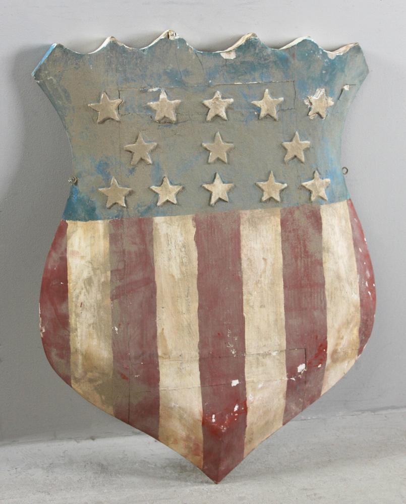 Folk Art Carved Wood and Painted Shield: Folk art carved wood and painted American flag shield, 31" x 23".