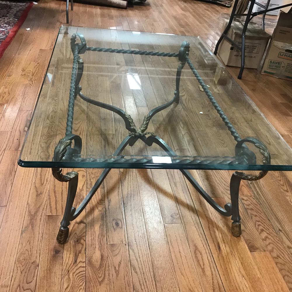 Fancy Wrought Iron Cocktail Table with Glass Top: Fancy wrought iron cocktail, occasional table with beveled glass top, having gold trim and hoof feet, 19" H x 54" W x 36" D.