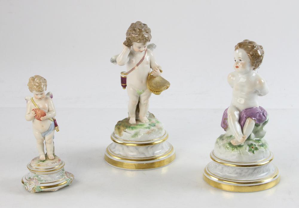 Three Meissen Cupid Figures: Late 19th/early 20th century Meissen figures of cupids, three total (3), all with faux marble bases to include one seated on grassy mound with his hands behind his back, one with basket and one holdin