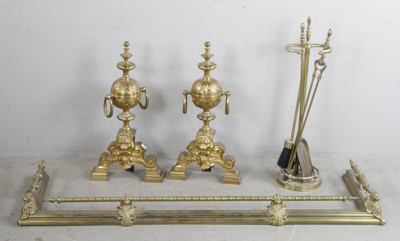Pair of English Brass Lion Head Andirons, Fender: Pair of English brass lion's head andirons, 24" H x 12" W x 5" D. Includes fender, 54" x 15", and tools. Provenance: Estate of August van der Becq, Westport, Connecticut.
