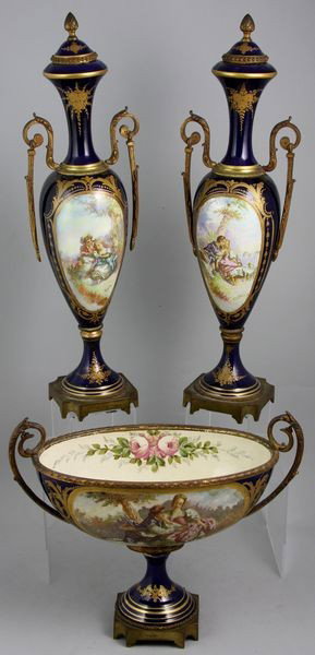 19th C. Sevres Three-Piece Suite: 19th Century Sevres three-piece suite which includes a hand painted porcelain center urn with handles and two (2) hand painted porcelain covered side urns, gold leaf over cobalt porcelain and ormolu m