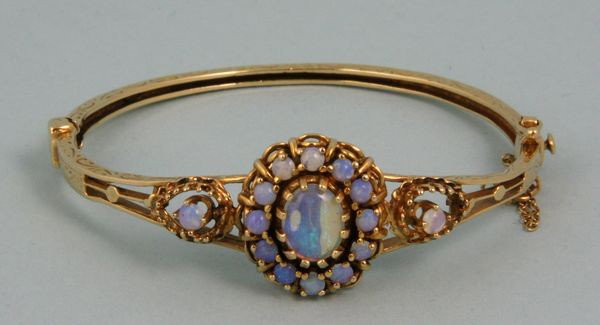 14k Opal Bangel Bracelet: 14k yellow gold, opal bangle bracelet, having fourteen (14) small opals and one (1) large center opal, marked "14k" on clasp, 0.5oz/10 dwt t.w., 1 15/16"h x 2 1/8"w. Good condition.