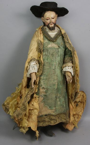 Carved Wood Santos Figure: Carved and painted wood santos figure, man in green tunic with black hat and gold robe, 25"h x 9"w (approx.) x 8"d (approx.). Paint loss, some fingers repaired, gold robe is extremely fragile and show