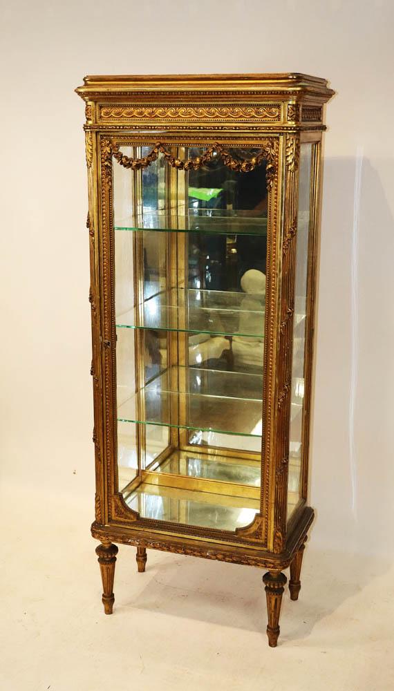 Louis XVI Style Giltwood Vitrine: Louis XVI-style giltwood vitrine having mirrored interior, three glass shelves, carved swag on door crest, glass sides, wave band, molded flared cornice, 68" H x 25" W x 15" D.