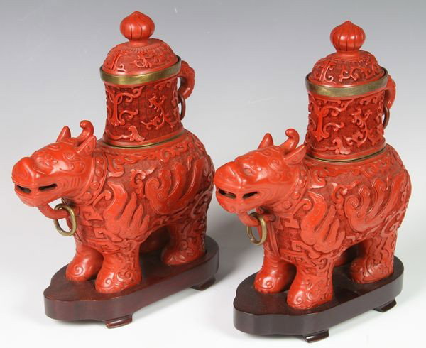 Chinese Pair of 20th C. Cinnabar Foo Dogs: Pair of cinnabar foo dogs, China, 20th century, decorated with scrolling motifs, fitted with containers on their backs, on wood stands, 8 1/2"h overall.