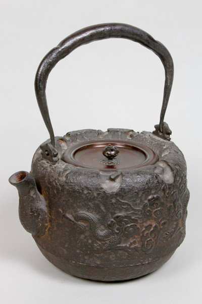 Japanese 19th C. Metal Teapot: Teapot, Japan, 19th century, metal, decorated with dragons amongst clouds in relief, the handle with silver inlays, bronze cover, signed, 11 1/2" x 8 1/2".