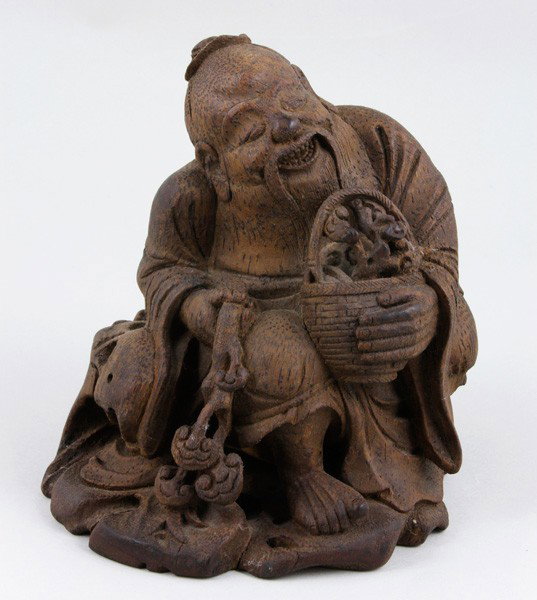 Chinese 19th C. Bamboo Figure: Figure of Cai Shen, China, 19th century, bamboo, the God of Wealth, seated and holding a basket full of ruyi in one hand and a ruyi scepter with multiple heads in the other, 6 1/4" x 6" x 5".