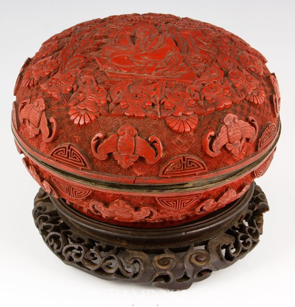 19th C. Chinese Cinnabar Box: Cinnabar box, China, 19th century, carved rounded form, with matching wood base, decorated with a carved elder surrounded by bats, 3 3/4” x 7”. Minor damage to rim.