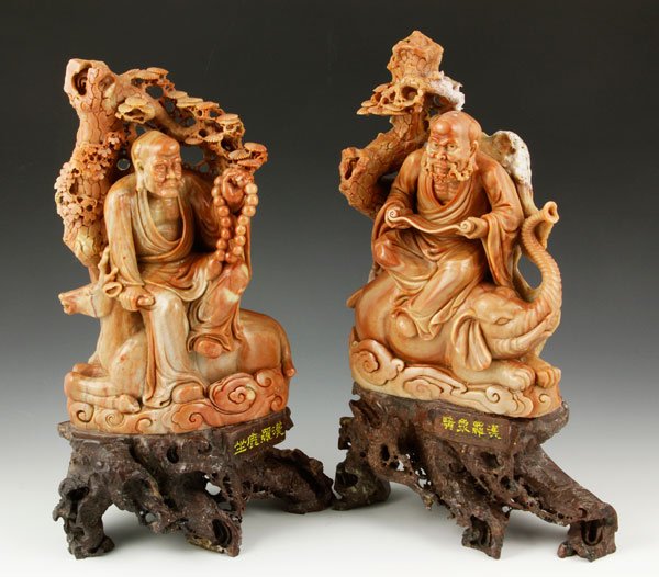 2 Soapstone Carved Luohan: Two luohan, China, carved soapstone, one seated on an elephant, one seated on a stag, both on root carved wood bases, 12 1/4".