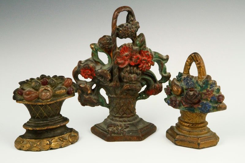 Lot of 3 Cast-Iron Doorstops: 3 cast-iron door stops, one 7 1/2" tall basket of red and green flowers with overhead handle and tall crisscross basket with 3-sided base, the second a basket of red and blue flowers and green leaves 