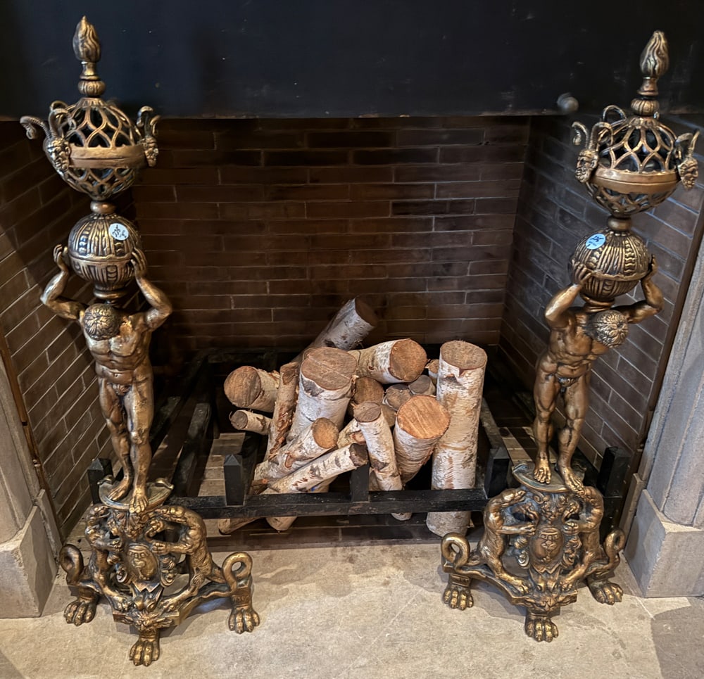 PAIR OF BAROQUE STYLE PATINATED-METAL ANDIRONS: A PAIR OF BAROQUE STYLE PATINATED-METAL ANDIRONS Each in the form of a Greek male holding aloft a globe and a pierced basket with stylized masks and raised on a coat-of-arms flanked by fantastic beast