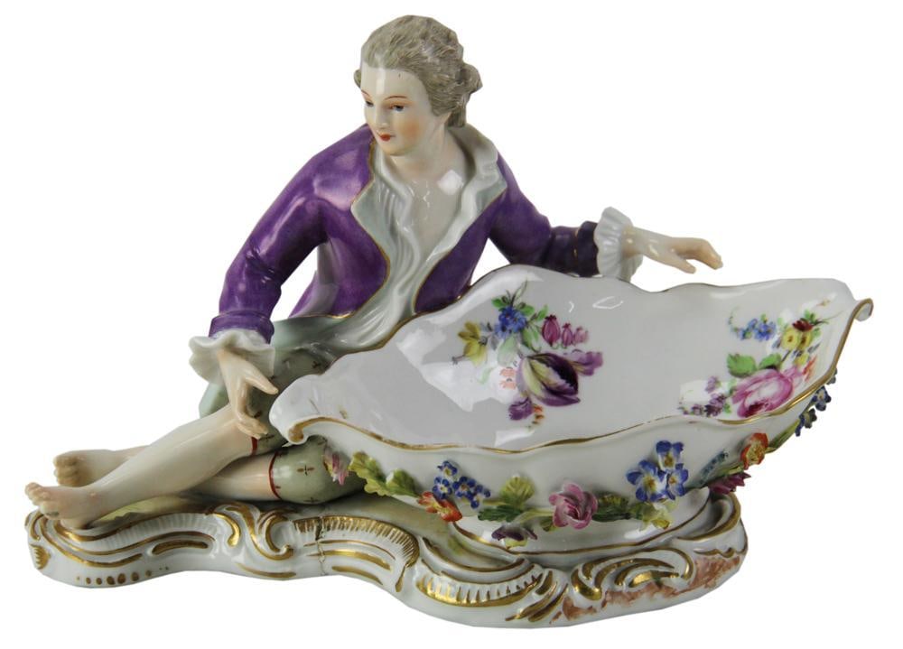 20thC Dresden Porcelain Male Holding Basket: 20th century Dresden porcelain male reclining figure holding basket of sweetmeats, 7" H x 11" L. Provenance: From the 50-year personal collection of Mr. John Hvozda of Hermitage, Pennsylvania.