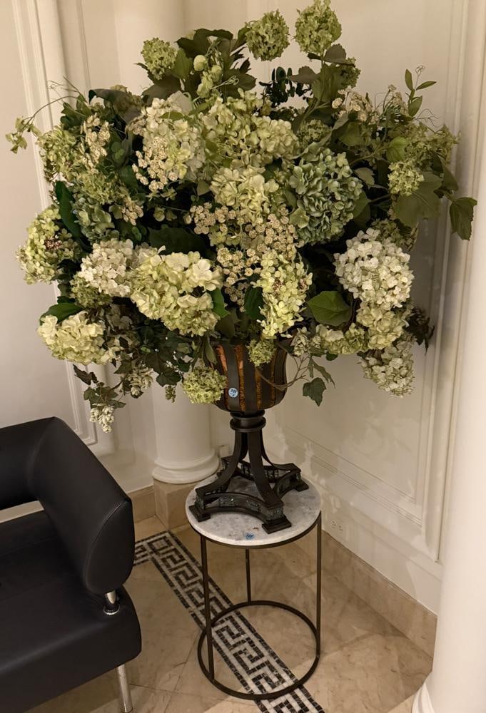Round Marble End Table and Floral Arrangement in Urn: Round marble end table together with a large artificial floral arrangement in an urn, 69" X 39" with flowers. Provenance: New York, New York. PLEASE NOTE: This lot is not from the Second