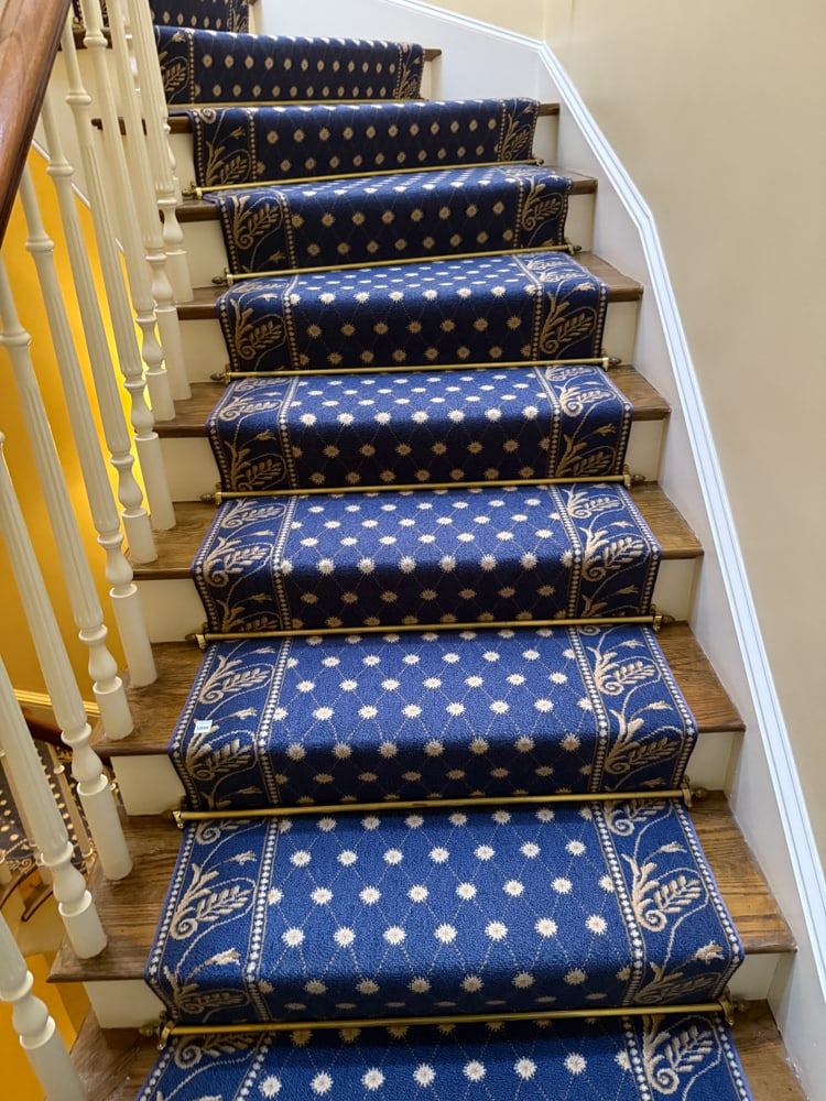 Custom-made Blue Staircase Rug with Floral Border: Custom-made blue staircase rug having a gold floral design on border. Includes brass stair rods. 2' 9" W, 4' 9" W at turn; 34' L. PLEASE NOTE: Item to be picked up at 129 Commonwealth Ave, Boston.