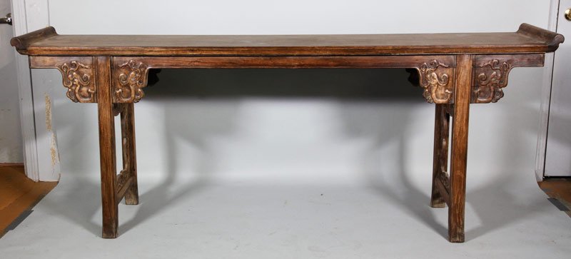 Chinese Huanghuali Altar Table: Huanghuali wood altar table, China, having a long rectangular top constructed from a single piece of wood with mythical beast head carved spandrels over four straight legs bridged by narrow side panel