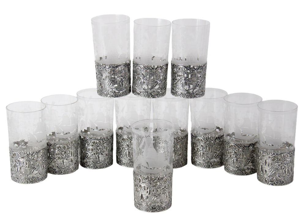 Set of Engraved Tumblers with Wyler Sterling Holders: Set of (12) tumblers engraved with windmill, ship, and florals, all with Wyler New York sterling holders, 5 3/4" H x 2 7/8" diameter. Sterling weight approximately 20.3 troy oz TW. Provenance: New