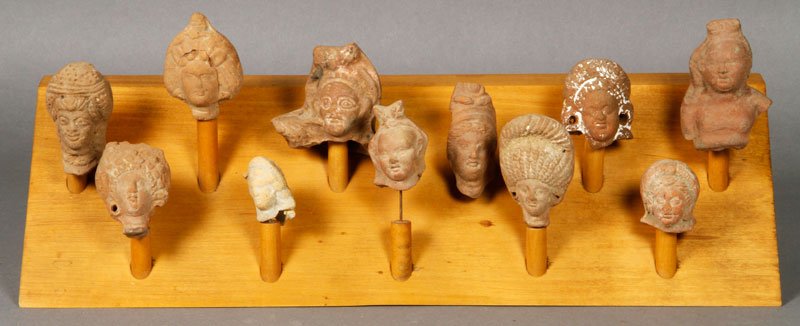Lot of Eleven Antique Pottery Figurine Heads: Lot of eleven antique pottery heads, most likely from Cambodia or Laos, with wood stands, most approximately 2" h. Provenance: From the collection of late Yale University professor Bernard Chaet.