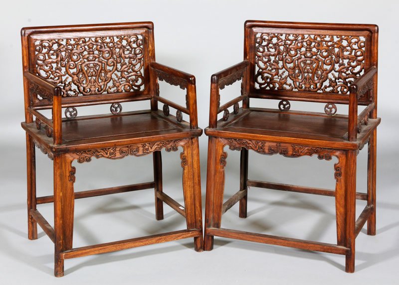 Chinese Pair of Huanghuali Chairs: Pair of Huanghuali wood armchairs, China, the back rest carved with a scrolling design incorporating two foo dogs on either side of a stylized lantern, the back and arm rest supported by carved mythic