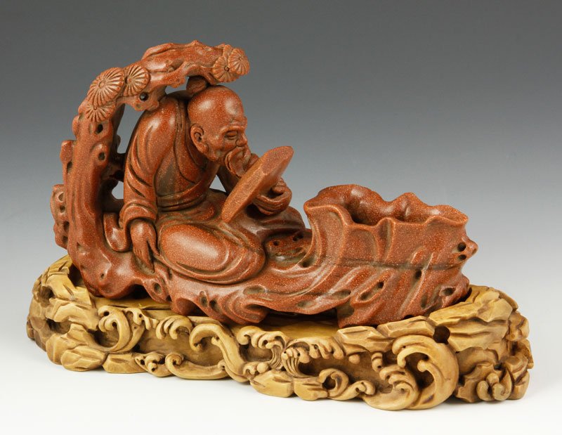 Chinese Golden Star Stone Figure: Carved golden star stone figure of a scholar reading under a pine tree, China, 18th century, on a matching carved wood base, 4 3/4" x 8 1/2". Provenance: From a private Massachusetts collection.