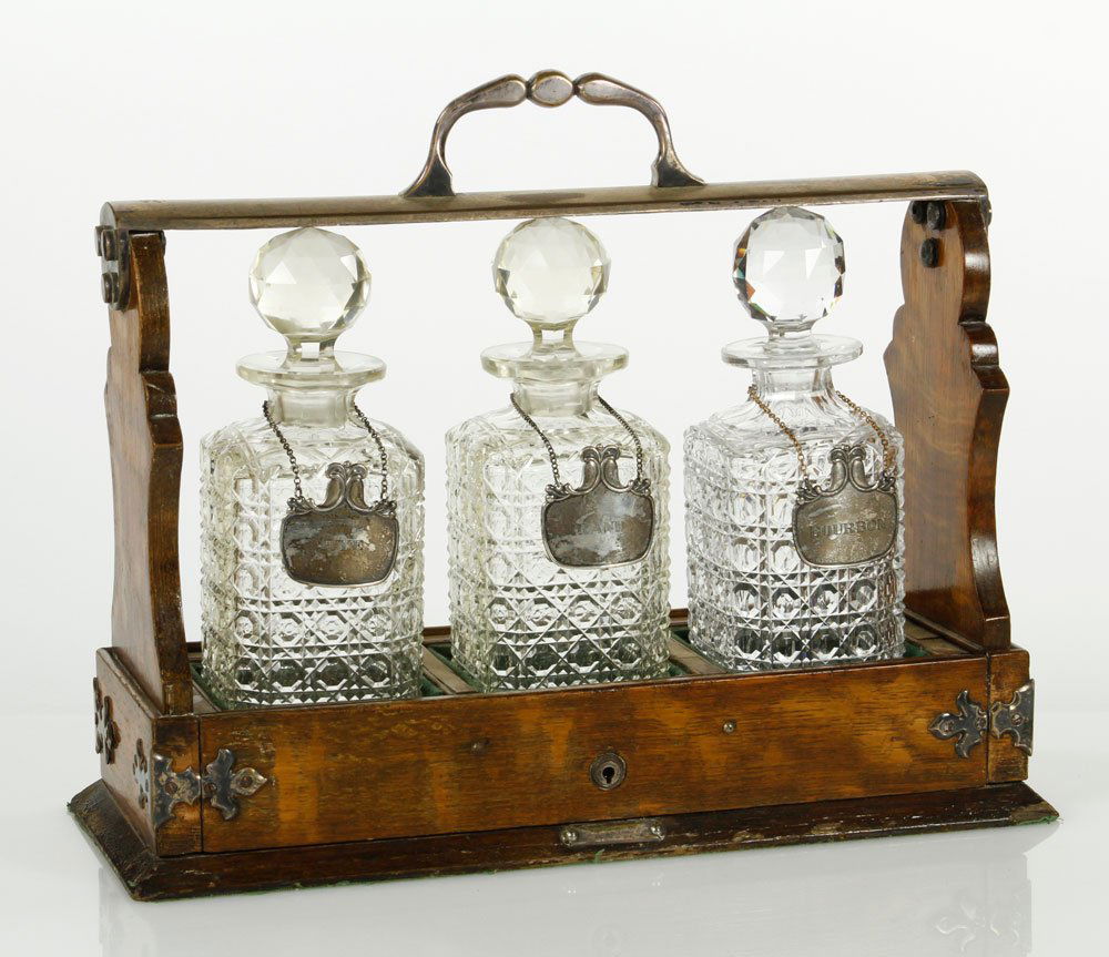 3 Bottle Tantalus: Silver plate-trimmed, three bottle tantalus in oak case by Mappin & Webb, three blown and cut liquor bottles and sterling tags, 13 1/2'' h x 16'' w. Provenance: Estate of Alexander Brook.