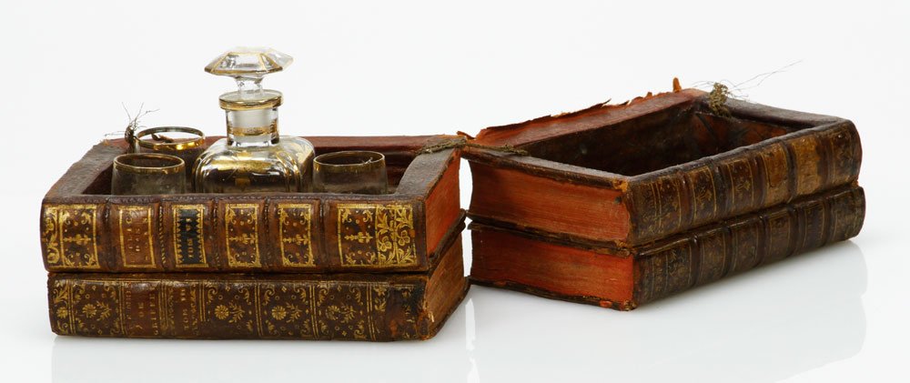 Leather Book Box with Decanter and Glasses: Leather book box holding decanter and 3 shot glasses, box 5" h x 6 1/4" w x 4" d. Provenance: Estate of Alexander Brook.