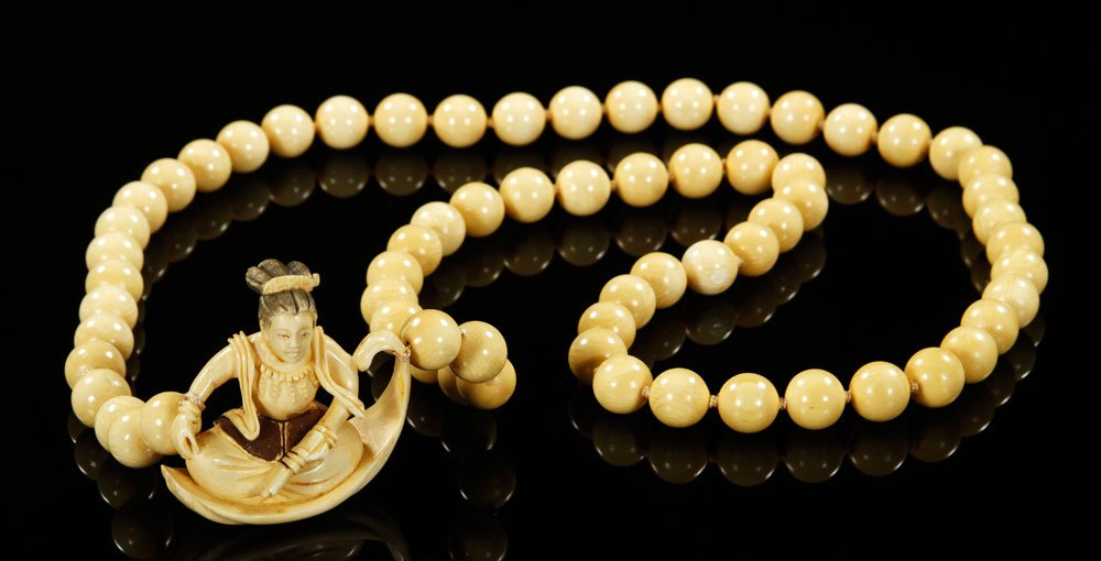 Japanese 19th C. Carved Ivory Necklace and Netsuke: Ivory bead necklace and netsuke, Japan, 19th century, hand carved ivory beads with a carved ivory netsuke figure seated in a reed boat, signed Gyoku Shi on base, netsuke 1 3/4" h, necklace 17" l.
