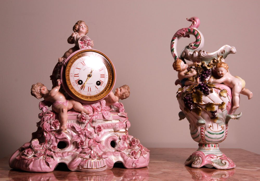 Antique German Porcelain Mantel Clock with Porcelain: Antique German mantel clock, porcelain, pink with putti figures, with key and pendulum, along with porcelain ewer with putti design, clock 12" h, ewer 13" h. Provenance: From the estate of the late Ra