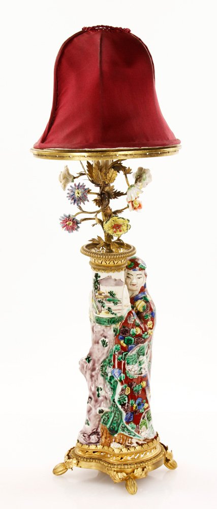 Chinese Figural Lamp: Lamp, China, body in shape of tree trunk with leaning figure in red robe, having ormolu mounts and topped with multicolored flowers, with maroon shade, 20" h overall.