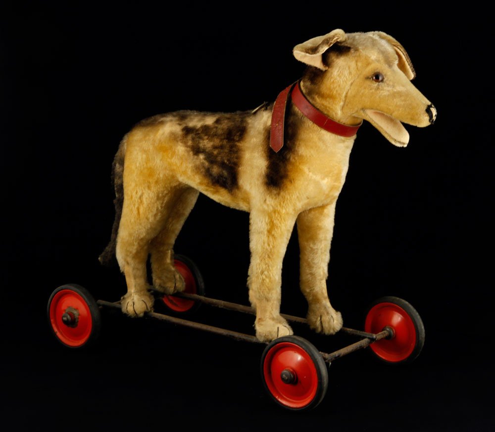 Steiff German Shepherd Pull Toy: Steiff German Shepherd pull toy, tan and black mohair, with growler, on red wheels, 22" h x 24" l. Provenance: From a Massachusetts estate.