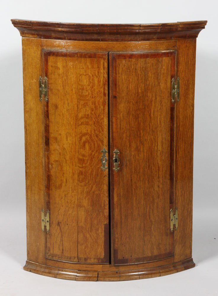 Late 18th C. Oak And Mahogany Corner Cupboard: Late 18th century oak and mahogany cross banded bow fronted mural corner cupboard, the molded cornice above a pair of cupboard door with exposed brass, 'H' hinges, enclosing three fixed shelves to the