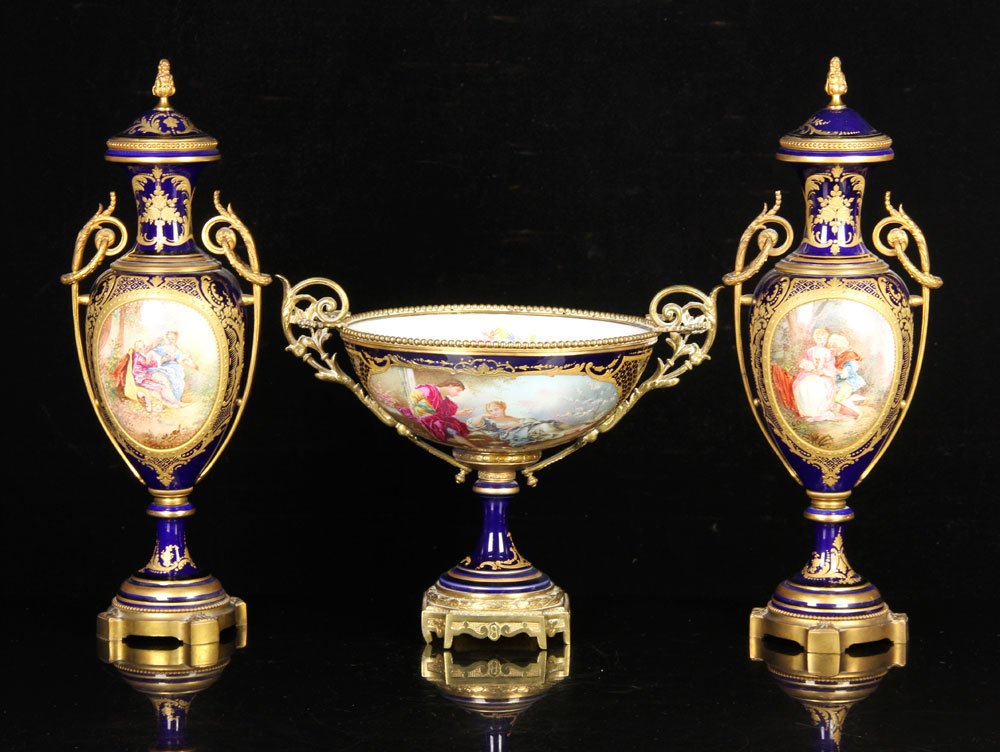 Sevres Three Piece Garniture Set: Sevres garniture set, three pieces, hand-painted with courting scenes, signed by artist, 18 1/2" h (urns), 11 1/2" h x 14" w (center bowl, across handles). Provenance: From a Massachusetts estate.