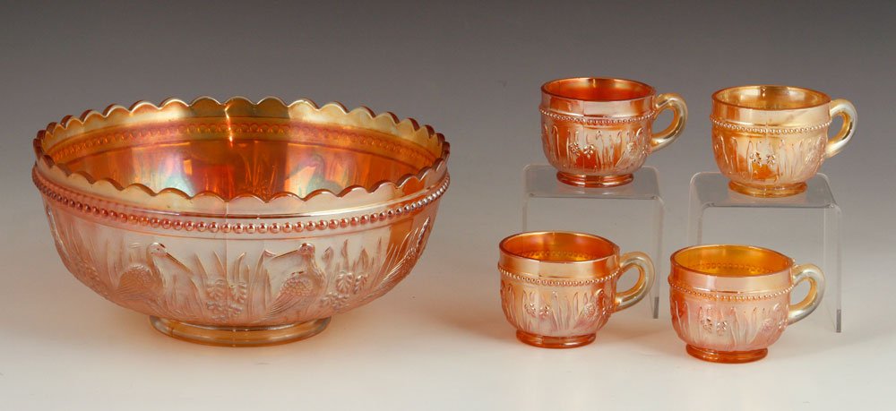 Marigold Carnival Glass Items: Lot of Marigold carnival glass items, in "Stork and Rushes" pattern, to include punch bowl and four cups with handle, bowl 4 1/2" h x 9 5/8" w. Provenance: From a California estate.