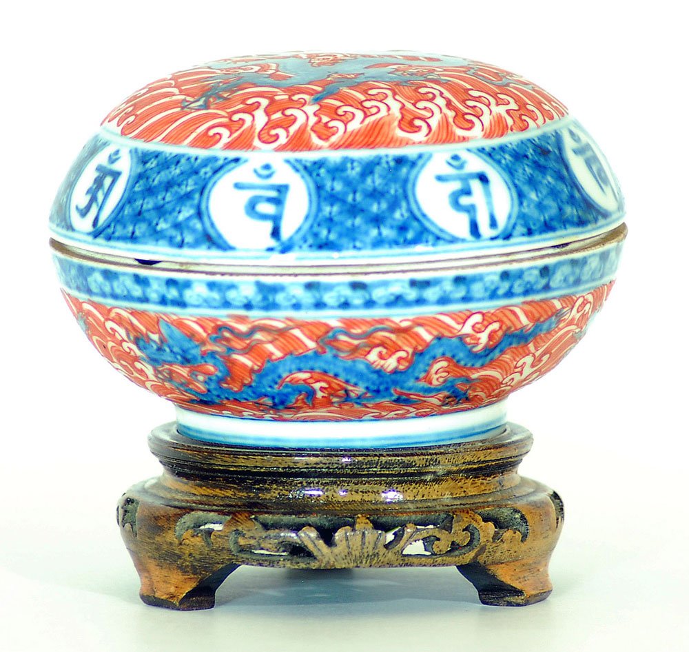 Chinese Iron-red Ink Box: Round porcelain box vividly depicting under-glazed five-claw dragons amongst bright iron-red waves, bordered with Tibetan Prayers, with Ming dynasty’s Chenghua reign mark on base, wood stand attache