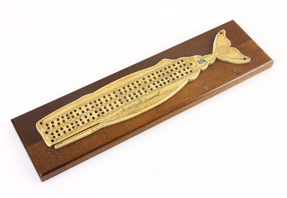 Whaling Cribbage Board: Whaling themed cribbage board, whale bone with mother of pearl inlay depicting a whaling scene, 13" long. Provenance: from the personal collection of Larry and Joy Redman of Lompoc, California.