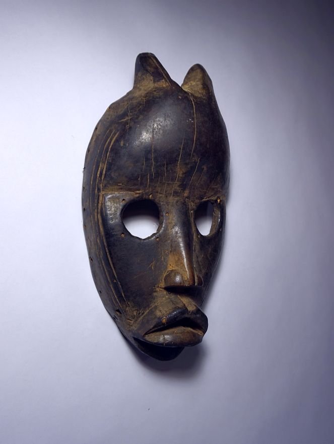 Old Dan African mask with horns, African Tribal Art: Incredible old Dan peoples mask from West Africa. Carved wooden mask with two small devil like horns and large open eyes, classic facial treatment. The mask is very well worn and with obvious field us