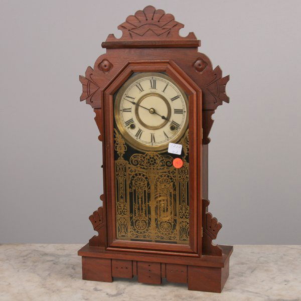 Late 1800 Victorian mantle clock," Ansonia", soli: Late 1800 Victorian mantle clock," Ansonia", solid walnut, incised carved crest, gilt decoration on glass, 21" tall 12" wide 4" deep. Later finish.